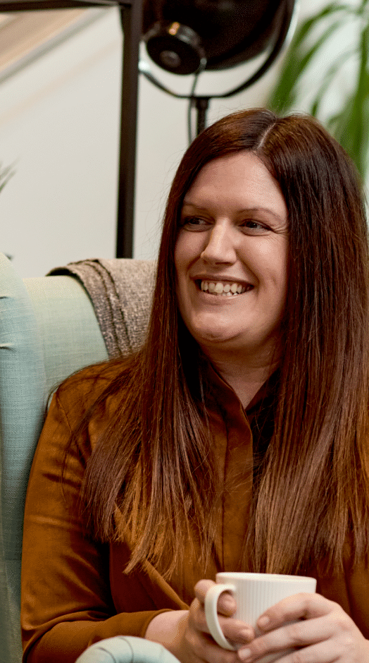 Two women sitting in chairs with a mug of tea smiling in conversation