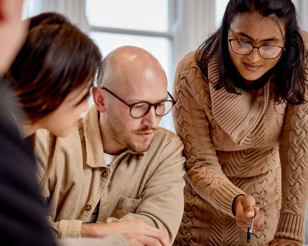 3 people gathering around looking at work on a desk