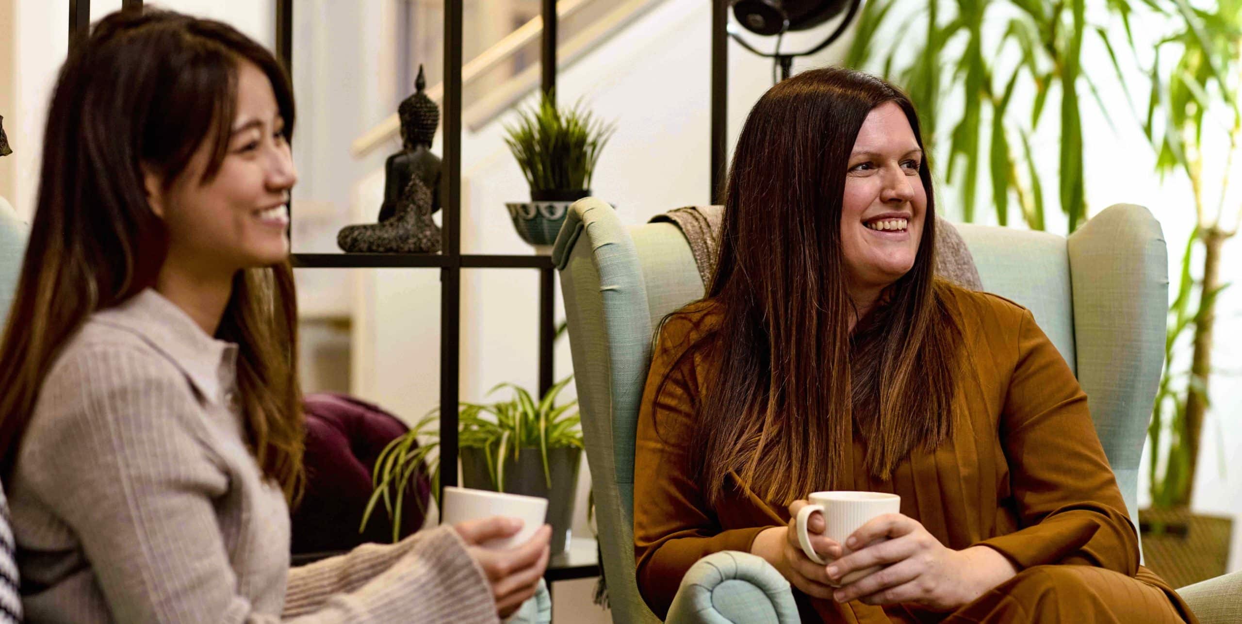 Two ladies sitting in armchairs with coffee and smiling